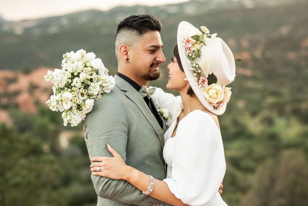 Romantic wedding couple embracing outdoors with white floral bouquet against mountain backdrop.