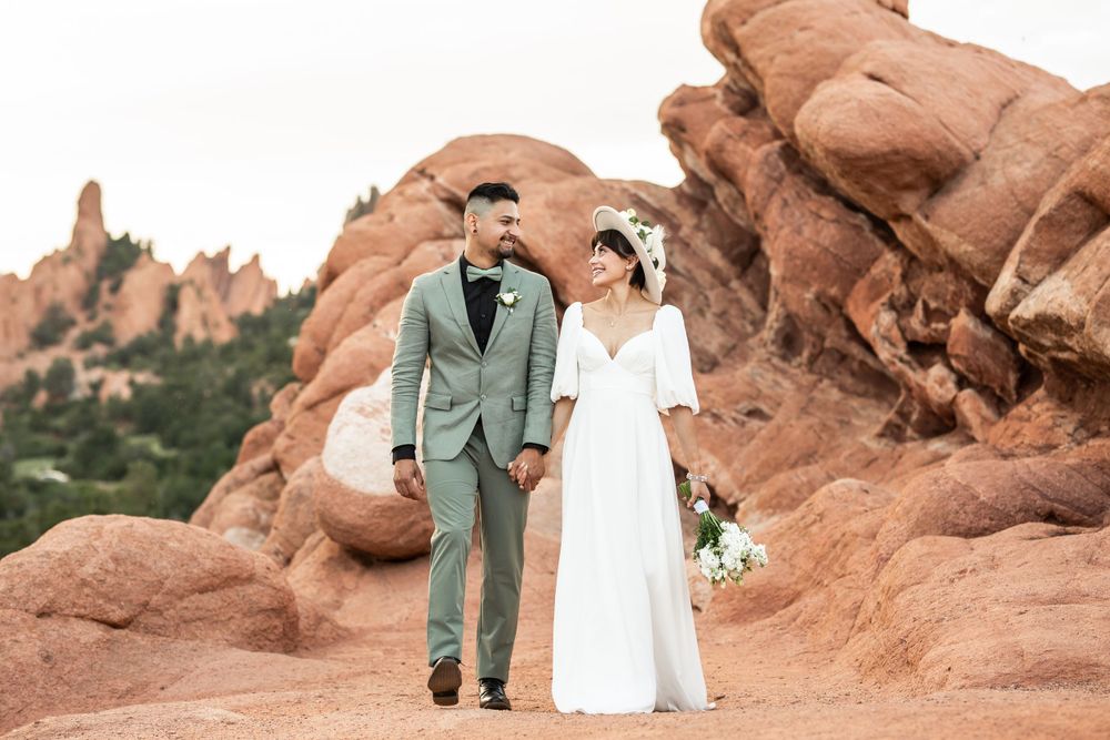 Wedding couple walking hand in hand among dramatic red rock formations.
