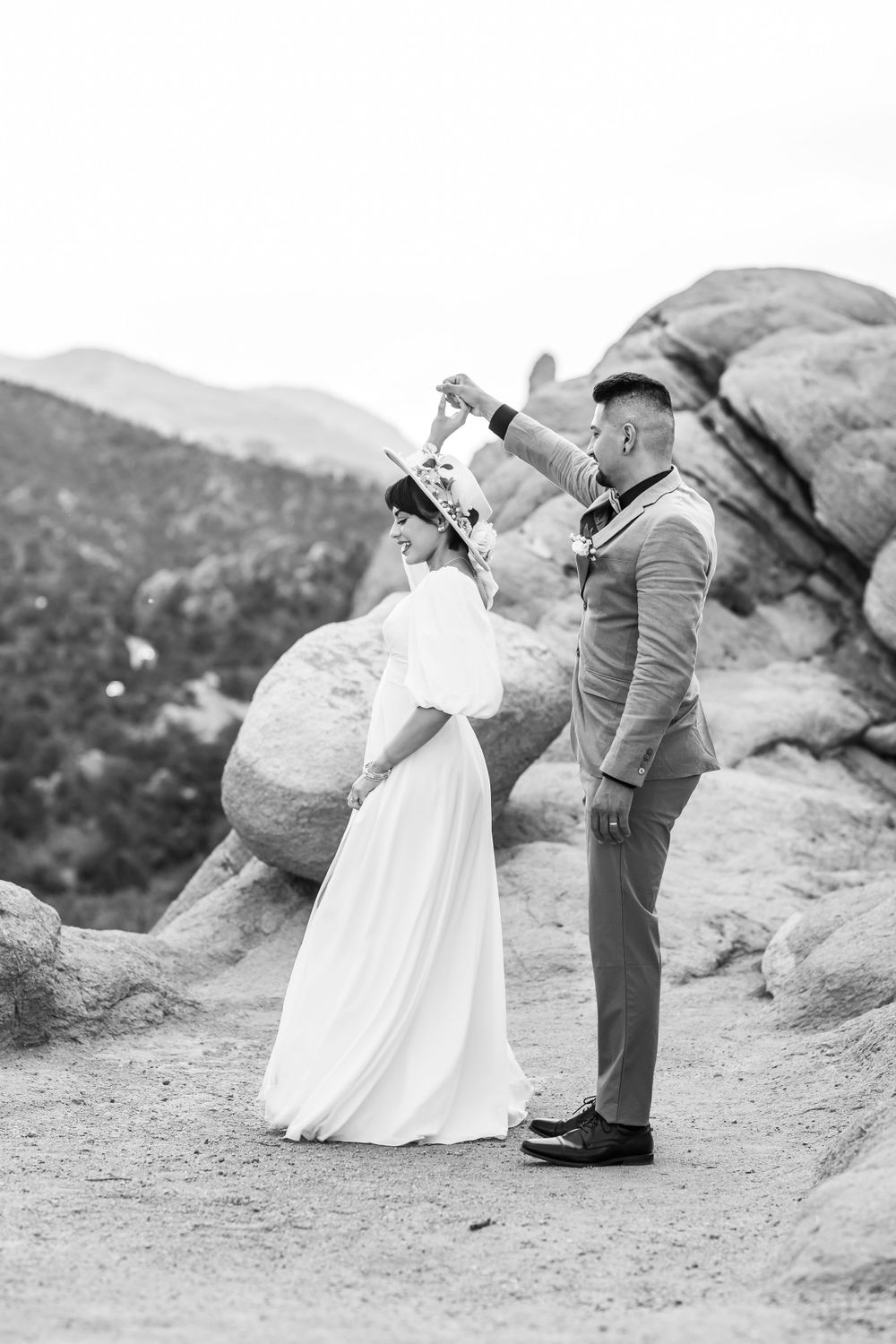 Black and white photo of playful wedding couple posing on rocky terrain.