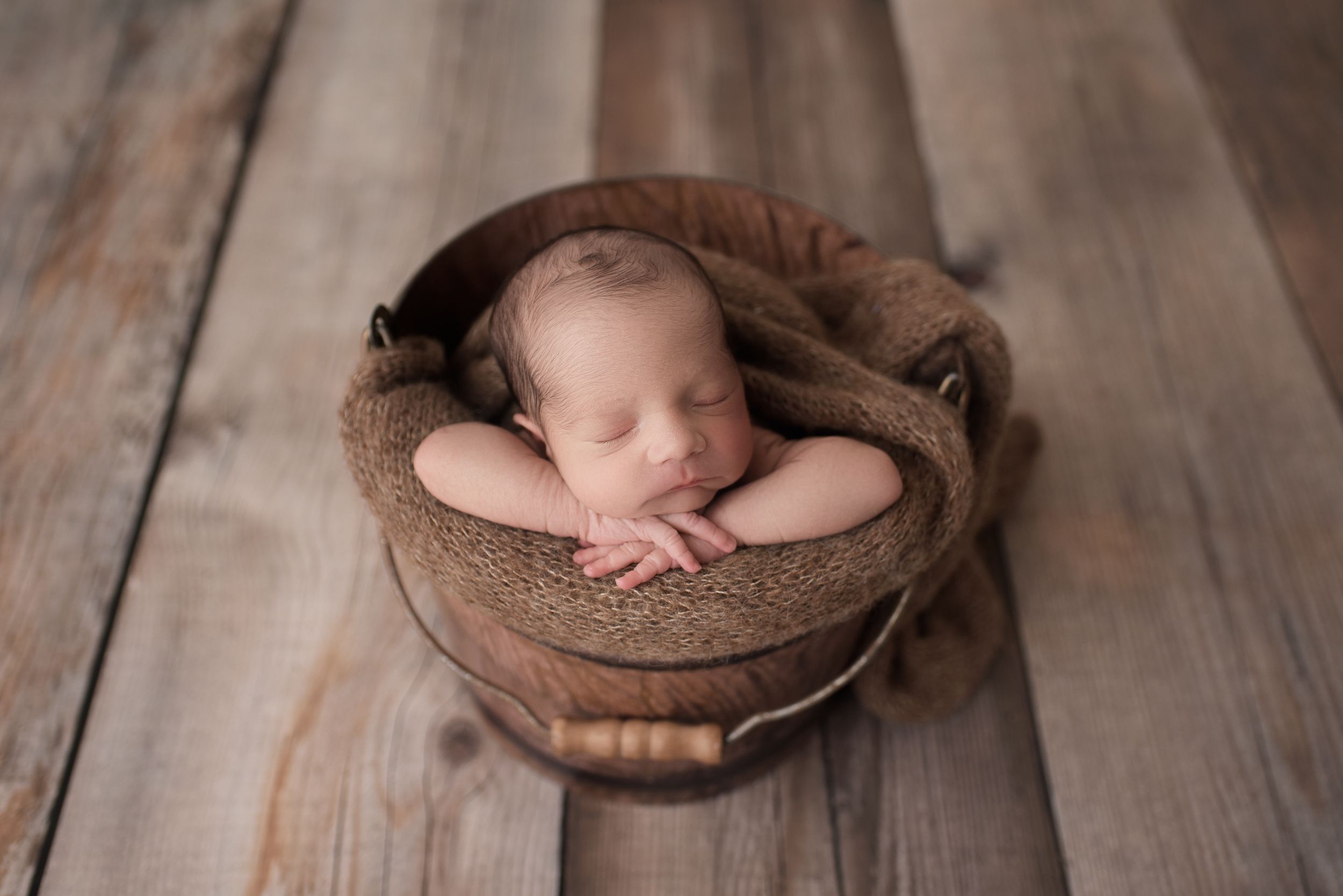 Newborn boy sleeping in a rustic bucket on a wood floor in Colorado Springs