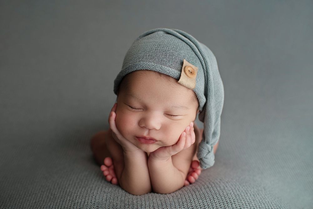 Newborn baby boy in the froggy pose on a dusty blue blanket wearing a matching sleepy cap