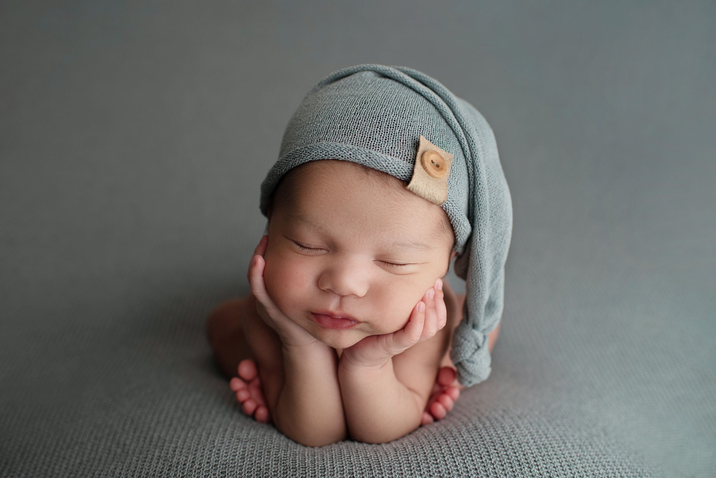 Newborn baby boy in the froggy pose on a dusty blue blanket wearing a matching sleepy cap