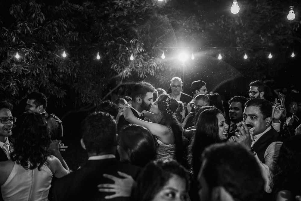 A crowd dancing under string lights at an outdoor reception, captured in black and white.