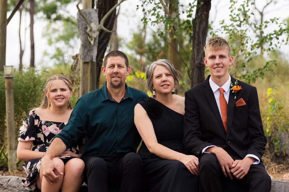 A group wearing black and formal attire poses together outdoors in front of trees and autumn foliage.