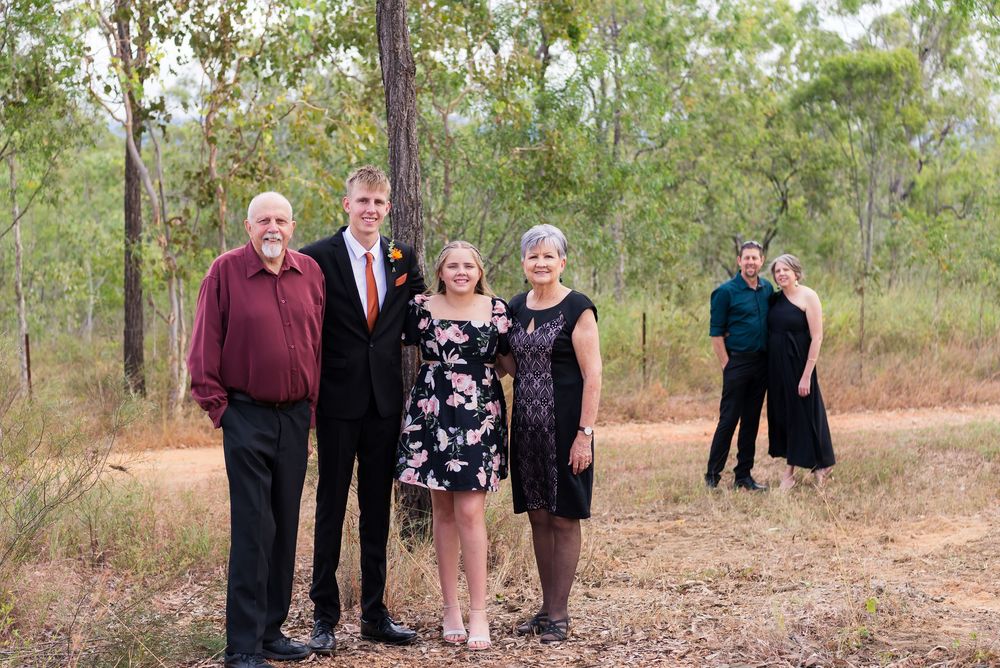 Family group portrait arranged in a line among trees in a natural outdoor setting.
