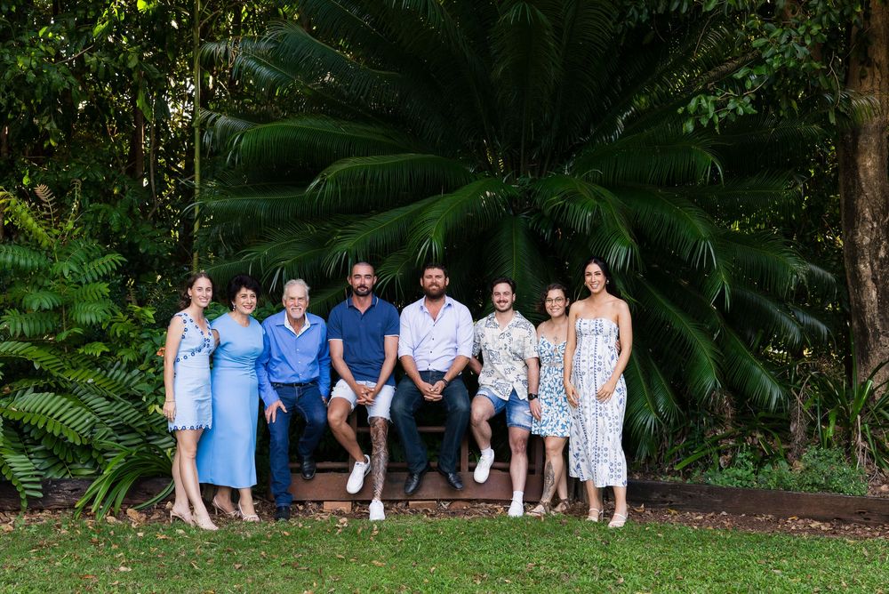 A group of people in coordinating blue and white outfits pose together in a lush garden setting for a photo shoot.