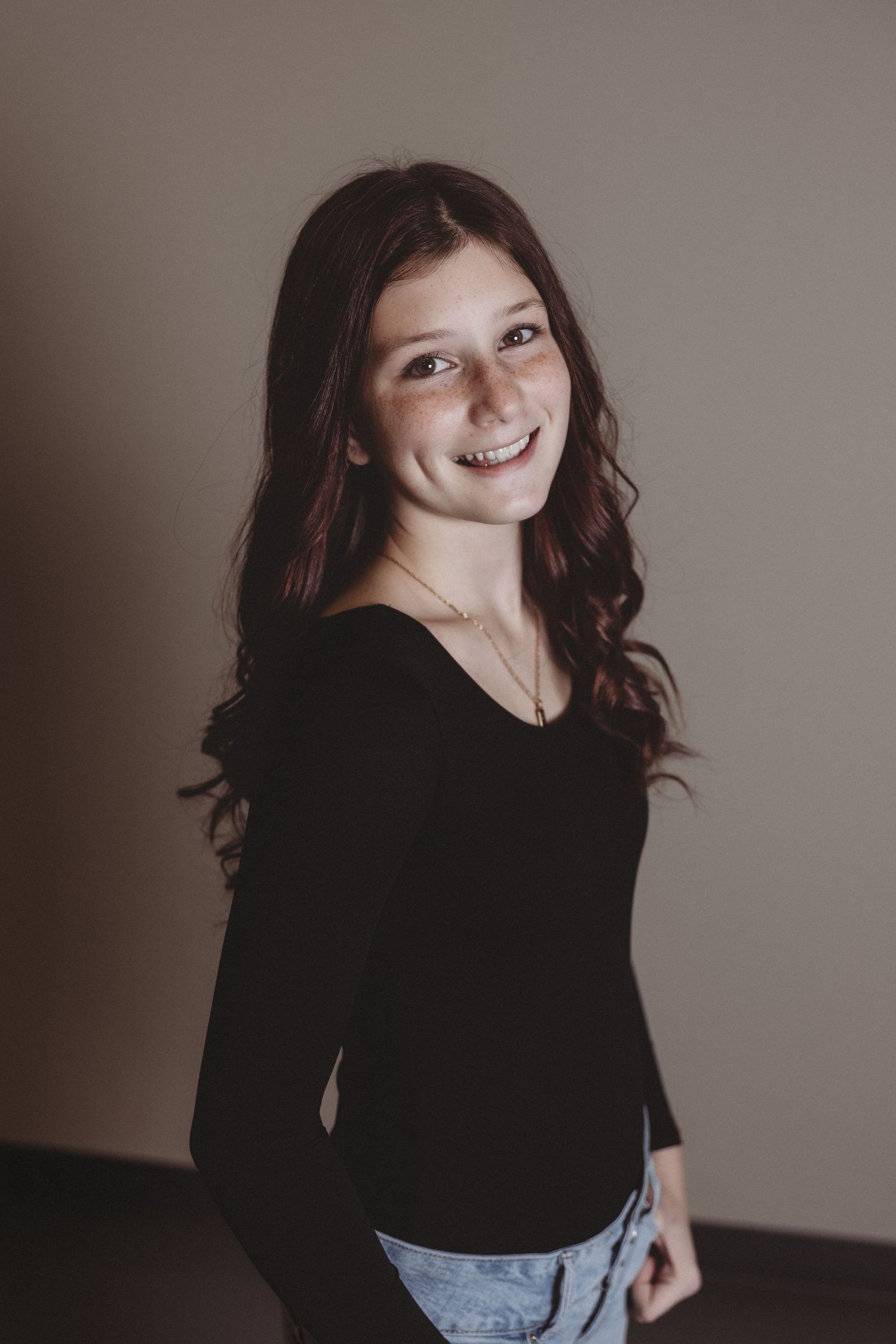 A portrait of someone leaning against a red brick wall with wavy brown hair and a blue top.