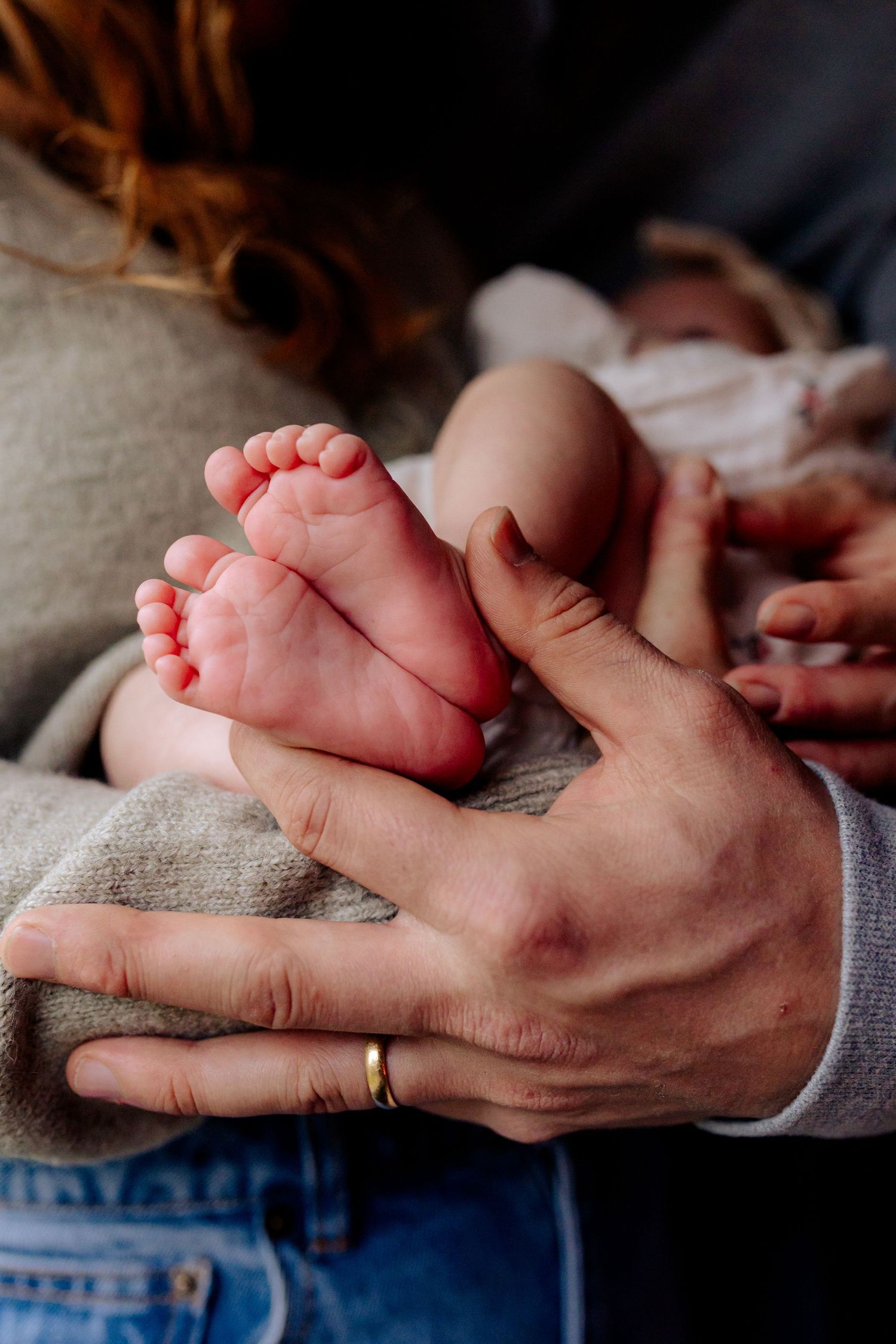 Parents cradling tiny newborn baby feet in their hands, with wedding ring visible, close-up family bonding moment.