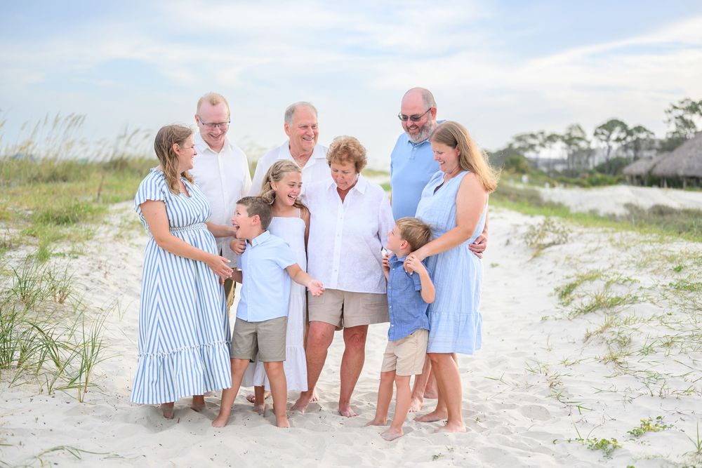 Multi-generational family portrait on sandy beach, dressed in blue and white, smiling together near sea oats.