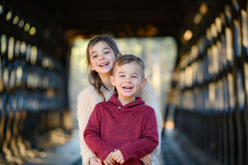A child in a burgundy hoodie smiles joyfully while posing outdoors against a blurred background.