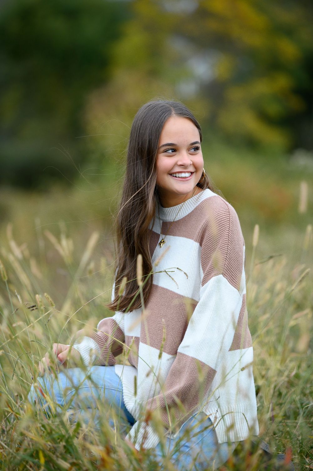 A person in a cozy sweater and jeans sits in a grassy meadow on a fall day.