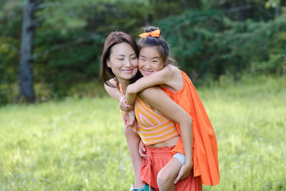 Two people share a joyful embrace while playing outdoors on a sunny day in a grassy area with trees in background.