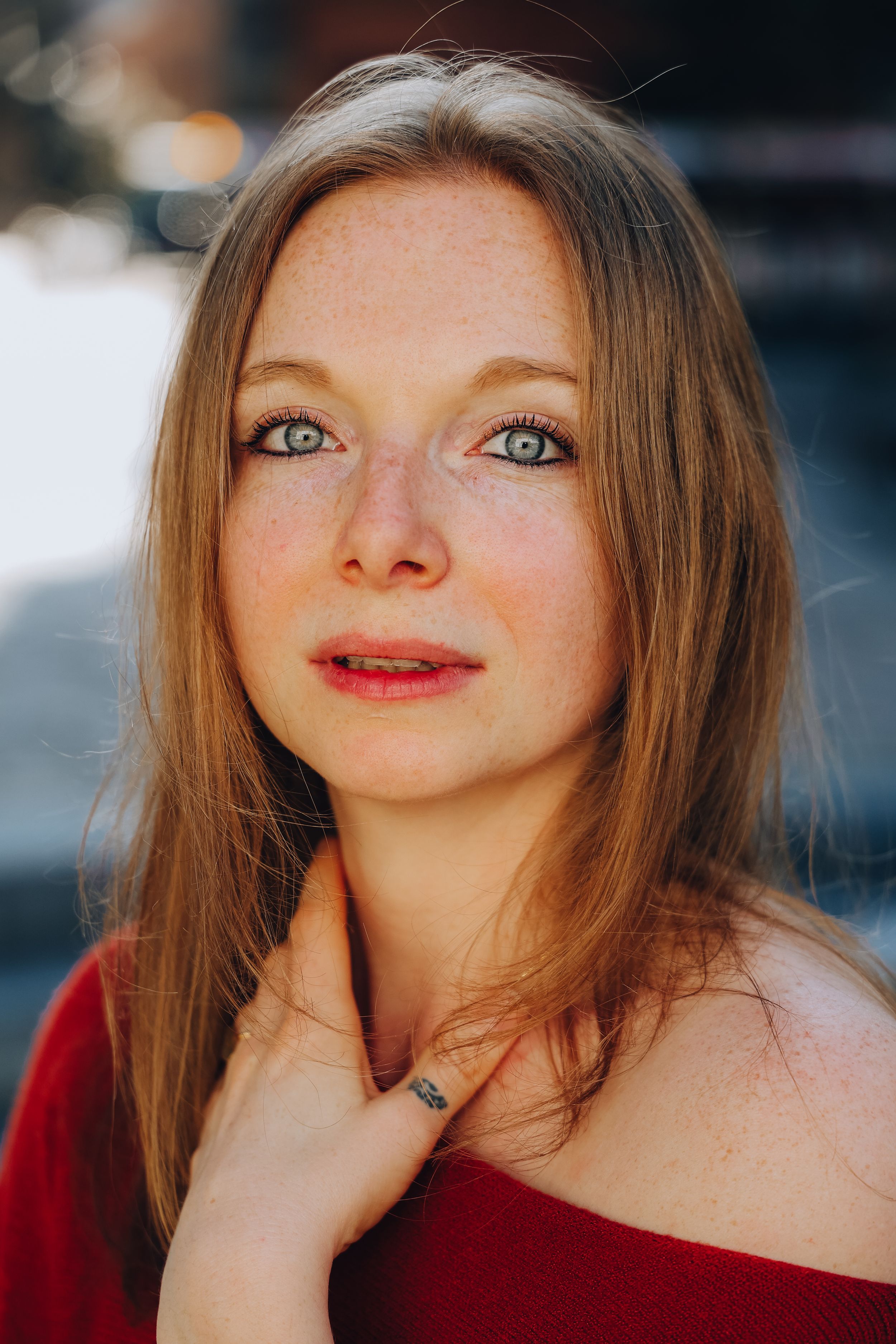 A young woman with freckles, blue eyes, and auburn hair wearing a red top gazes softly at the camera.