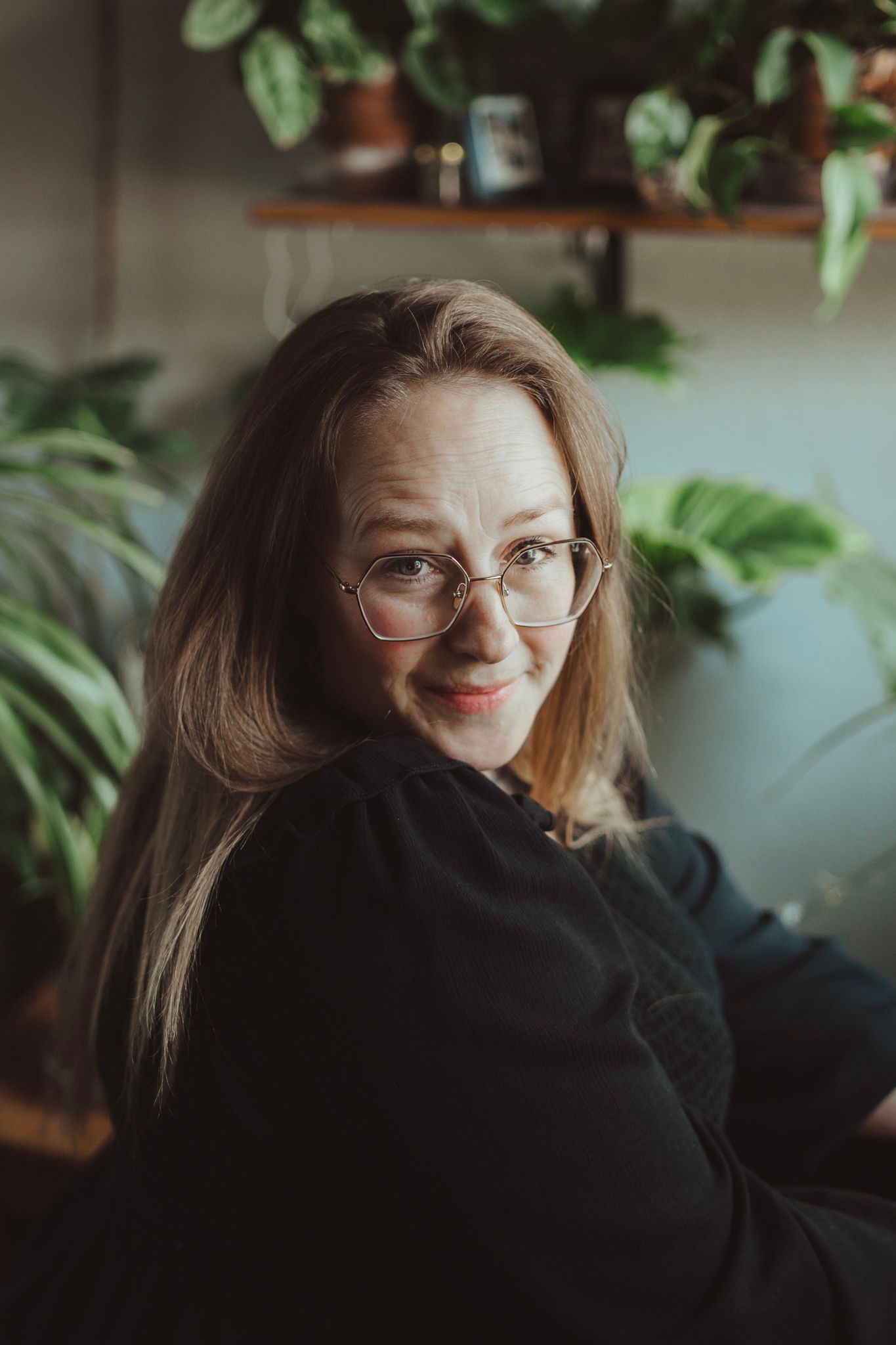 Portrait in cozy indoor setting with houseplants and warm lighting.