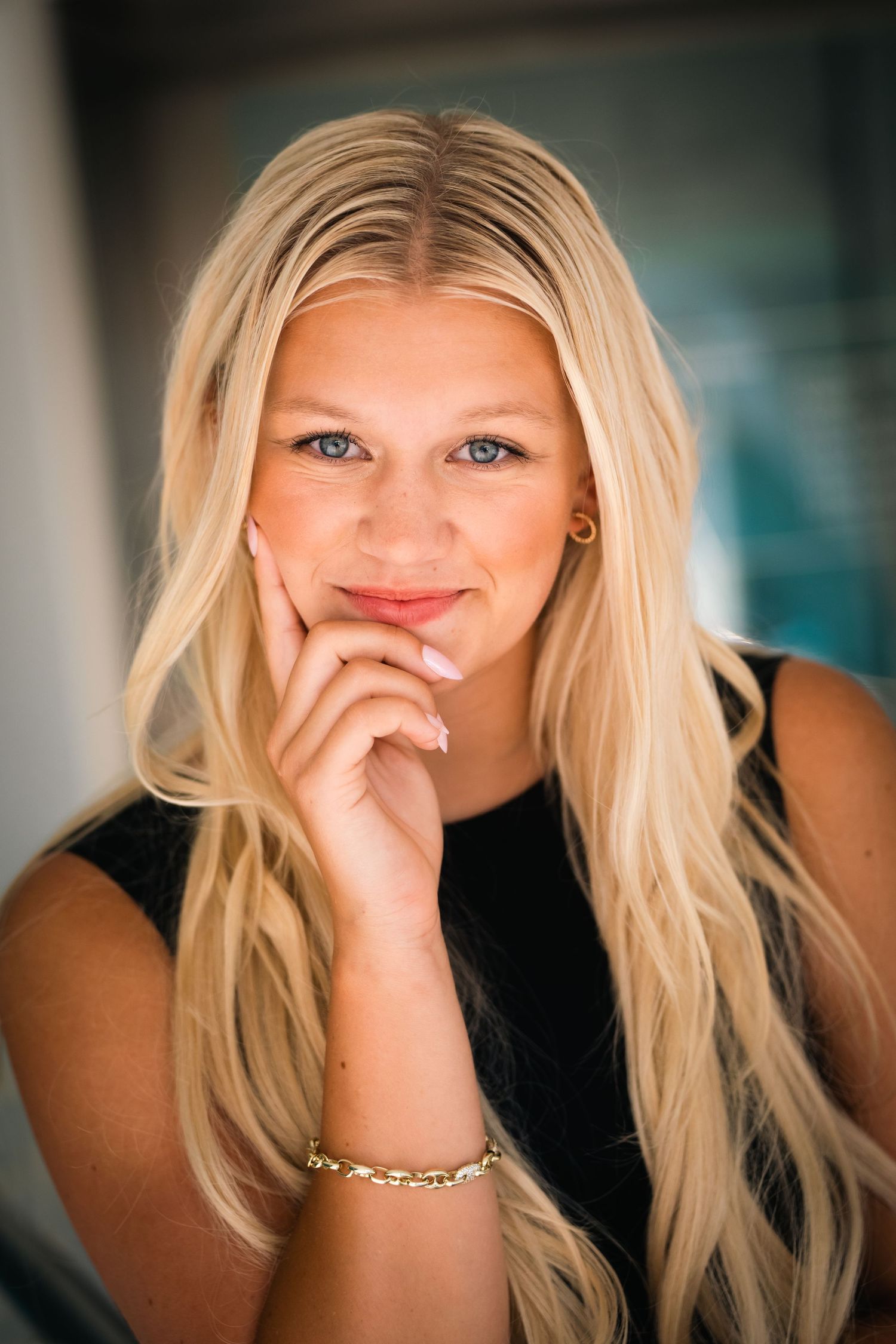 Portrait of a woman with long blonde hair and a black sleeveless top smiling while resting her chin on her hand.