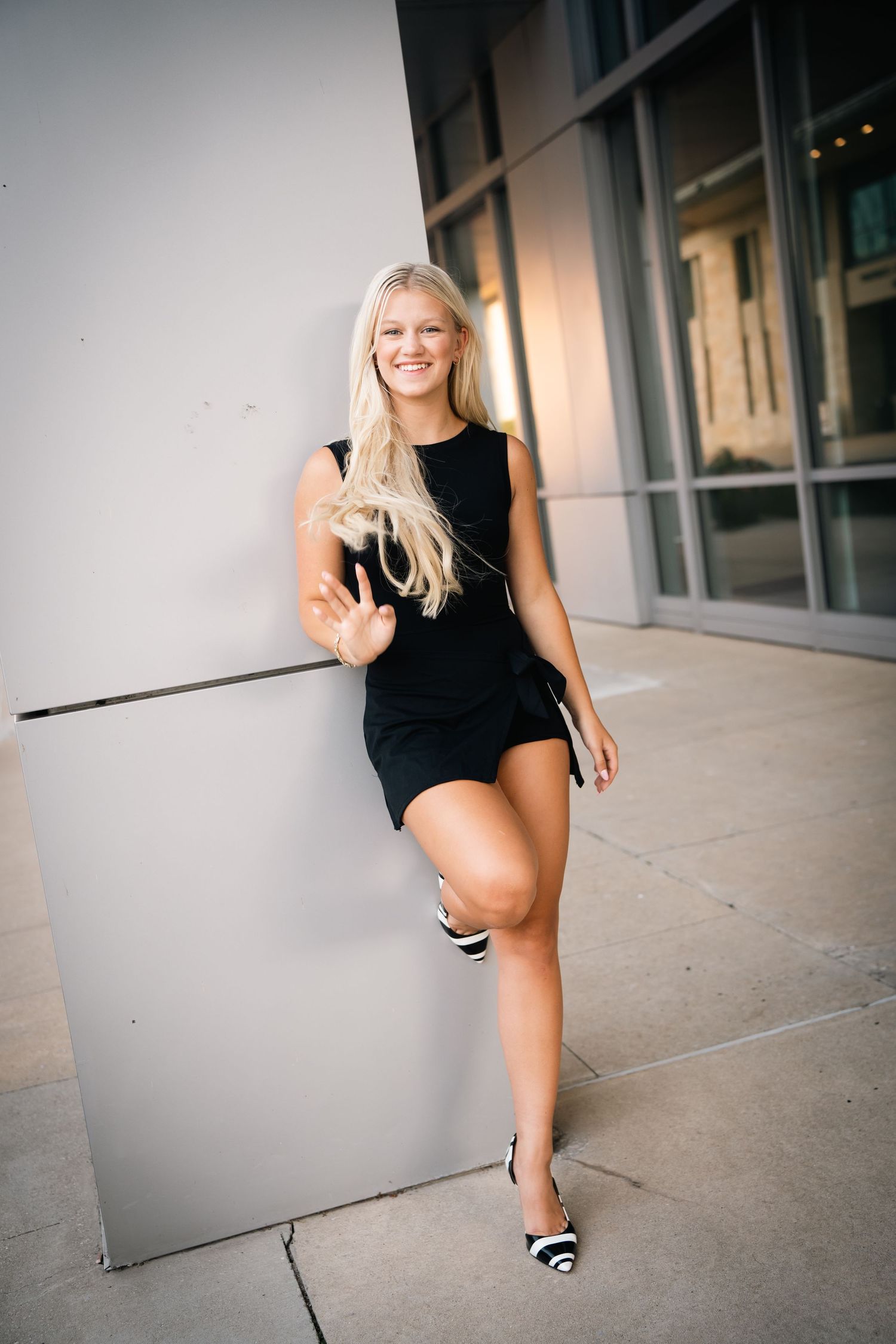 A person in a black sleeveless dress poses playfully in a series of connected photos against a modern building exterior.
