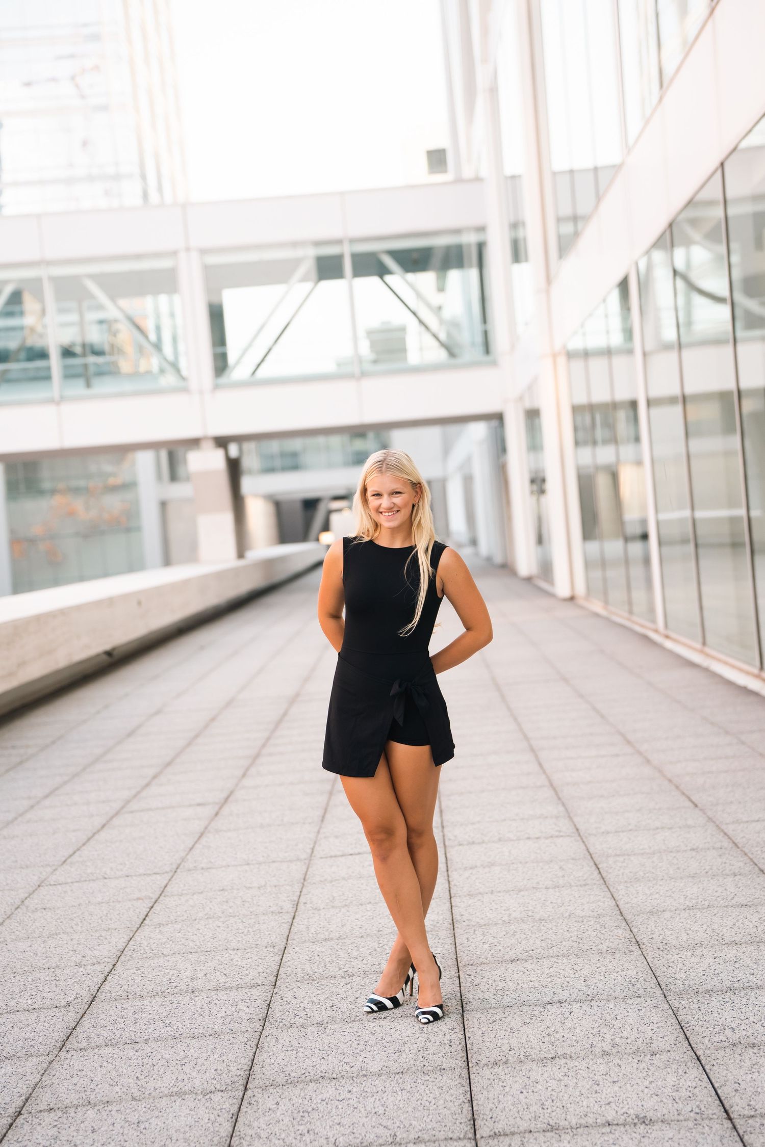 Dancer in black leotard performs graceful poses on tiled floor in bright modern hallway.
