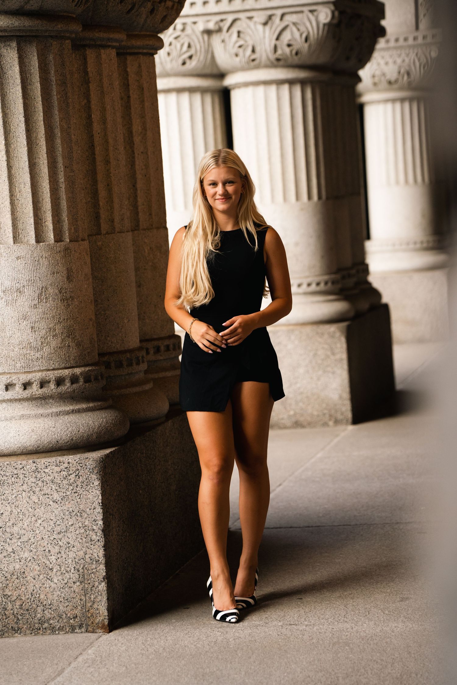 A series of architectural columns creates a dramatic colonnade with a person sitting on the ground between them.
