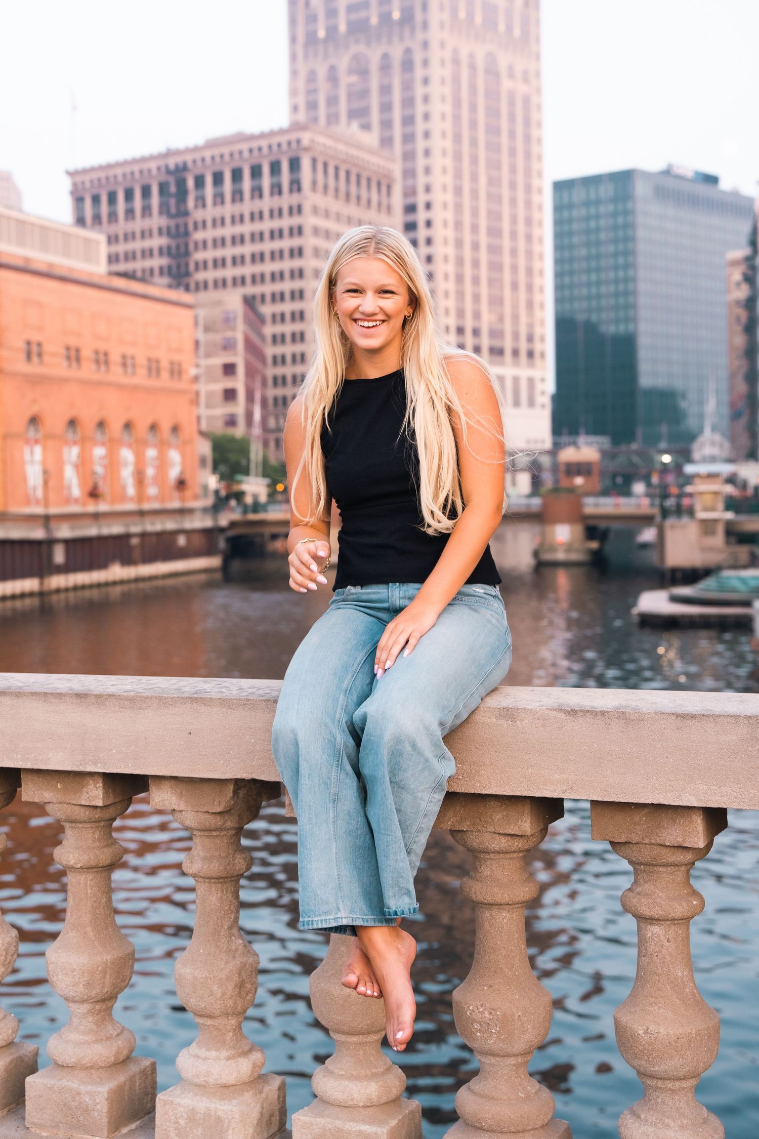 A series of four photos showing someone sitting on a stone railing overlooking Milwaukee's downtown riverfront at sunset.