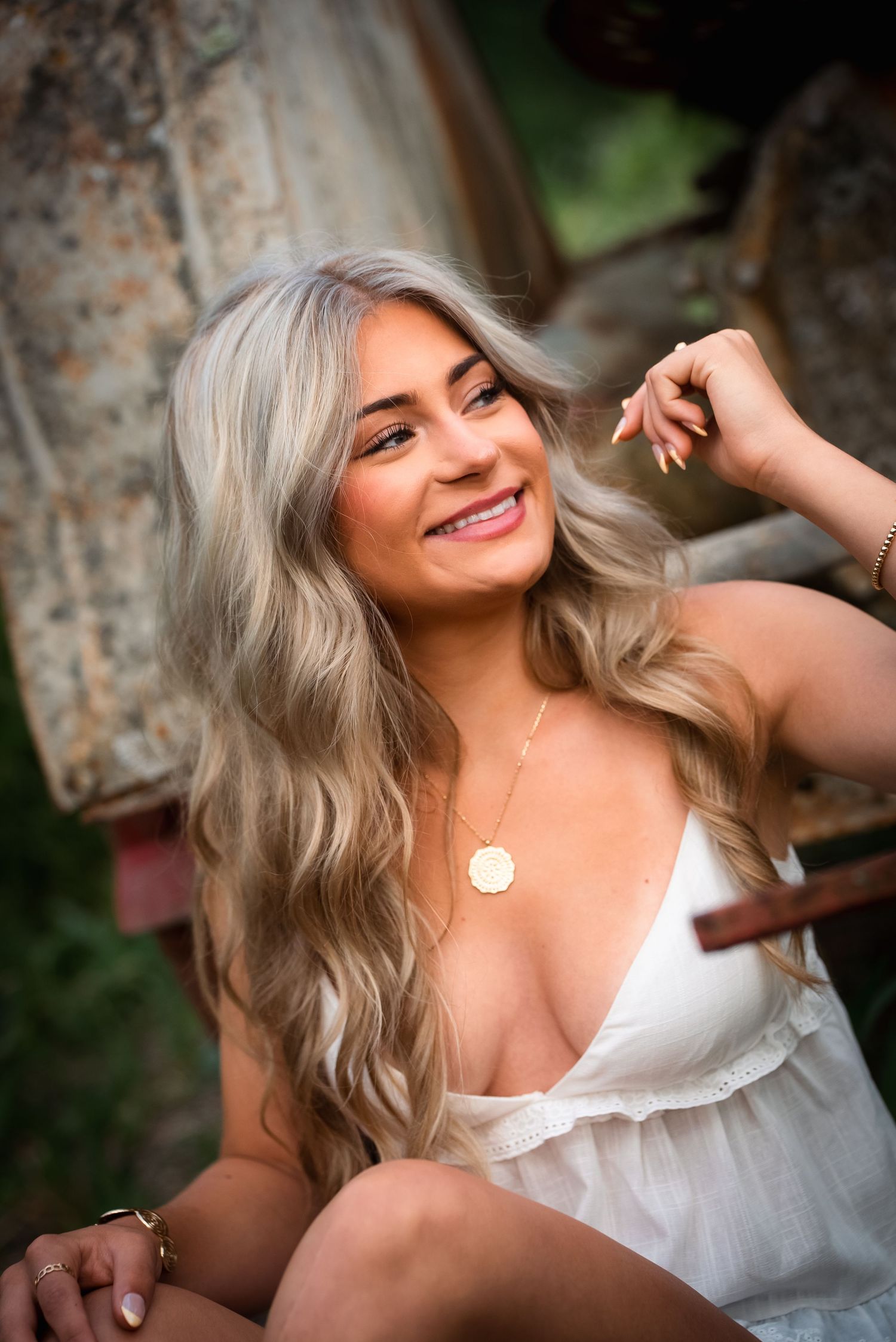 Portrait of a person in a white summer dress posing outdoors with vintage rustic equipment in the background.