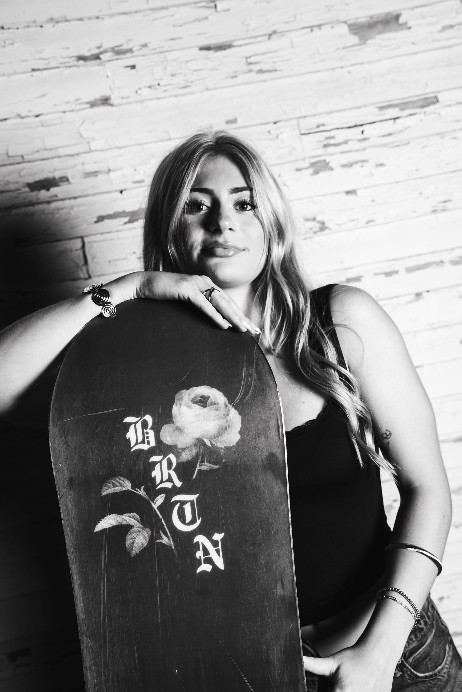 A series of black and white artistic photographs featuring a skateboard with a rose design against a white brick wall.