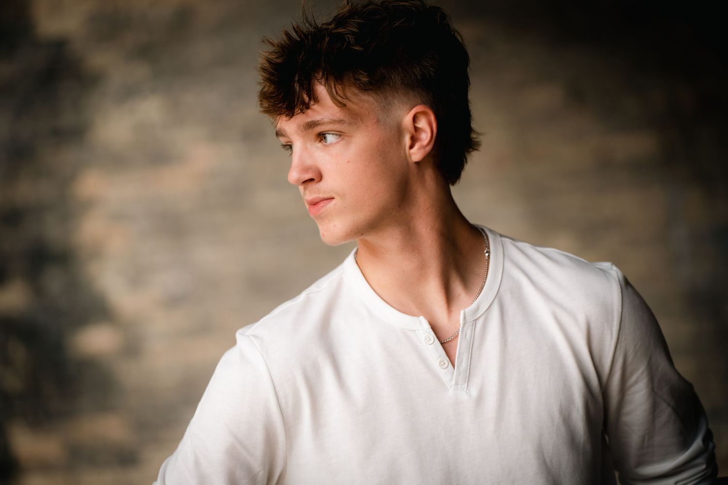 A person wearing a white shirt poses against a dark textured background in a dramatic studio portrait.