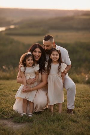 Family in coordinating white and cream outfits pose together on grassy hill during golden sunset.