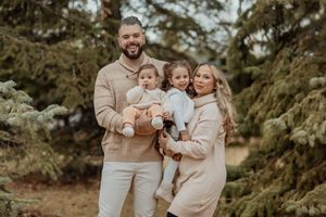 A joyful group dressed in neutral tones embraces and laughs together in a lush outdoor setting during golden hour.