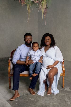 A loving family of three poses on a wooden bench against a gray backdrop in coordinated white and navy outfits.