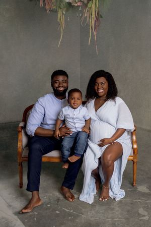 Family portrait on wooden bench wearing coordinated white and navy blue outfits against gray backdrop.