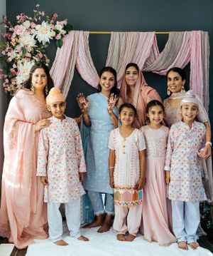 Group photo with traditional South Asian attire against floral backdrop and pink drapes.