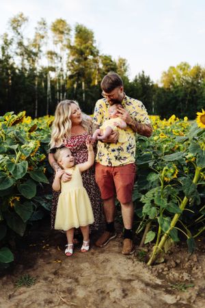 Family shares a tender moment together while standing in a beautiful sunflower field at sunset.