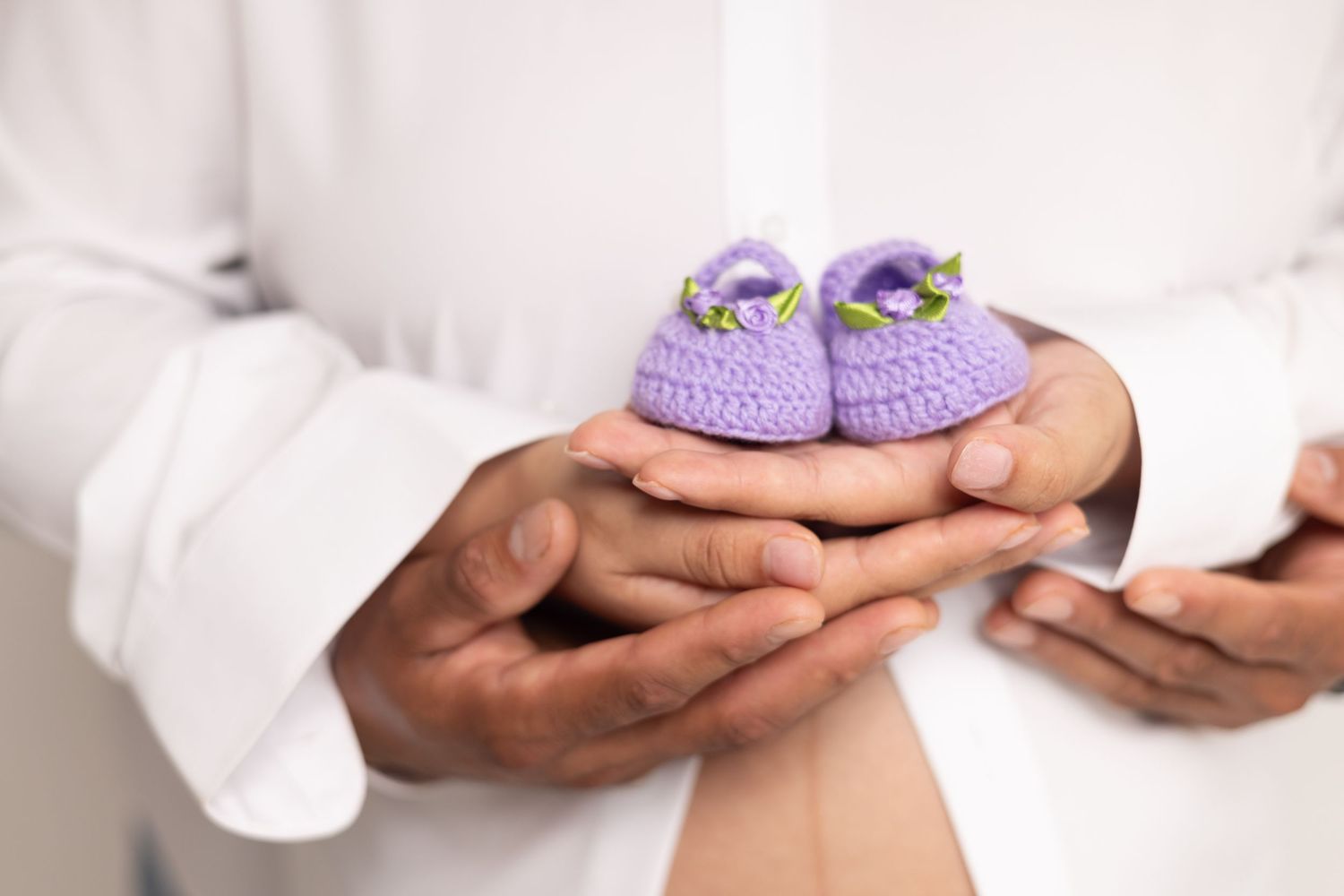 Couple holding tiny purple crocheted baby booties, symbolizing pregnancy and parenthood anticipation.