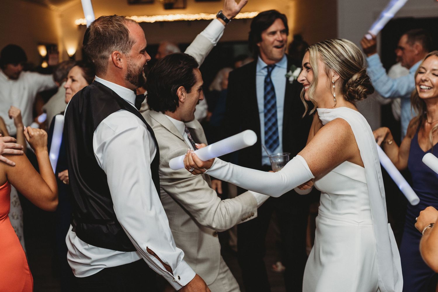 Bride and wedding guests celebrating on the dance floor with foam light sticks.