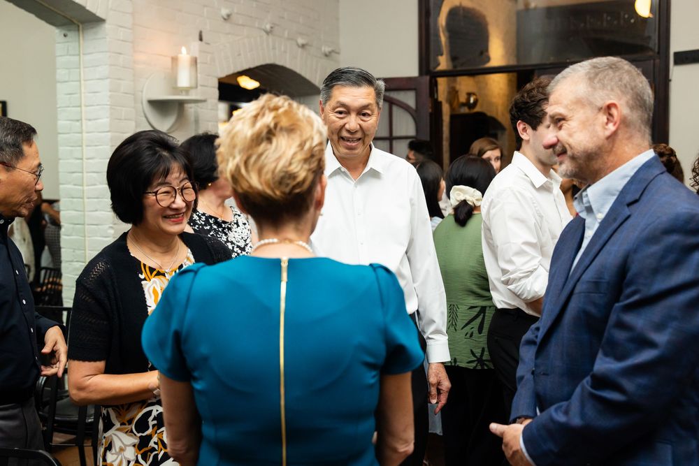 Group of professionals networking and socializing at an indoor event, smiling and engaged in conversation.