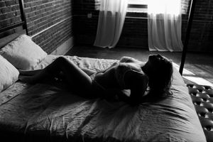Black and white photo of woman lying on bed in lingerie with natural window light.