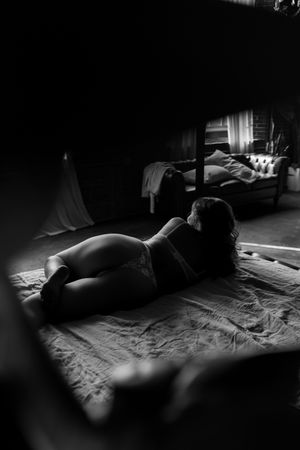 Woman in lingerie lying on floor in moody black and white boudoir photography with dramatic lighting.