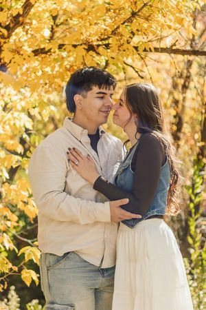 A young couple shares a romantic moment surrounded by vibrant yellow autumn foliage in a sunny park.