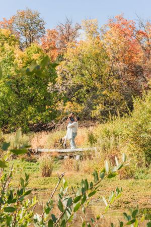 Couple embracing on a wooden dock surrounded by vibrant autumn foliage in a serene nature setting.