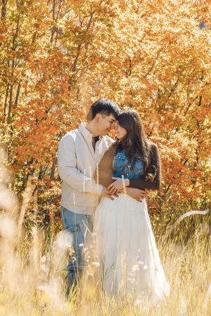 Couple embracing in autumn forest with vibrant orange foliage, woman in white dress and denim jacket.