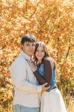 A young couple embracing and smiling in an autumn park with vibrant orange and yellow foliage in the background.
