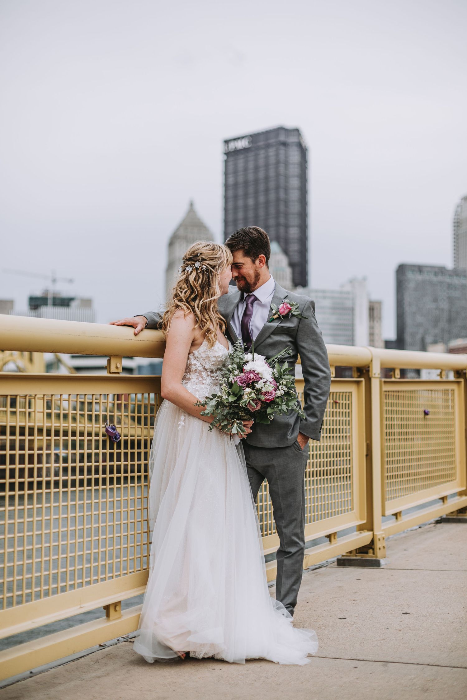 Bride and groom share a romantic moment on a yellow bridge with Pittsburgh city skyline in the background.