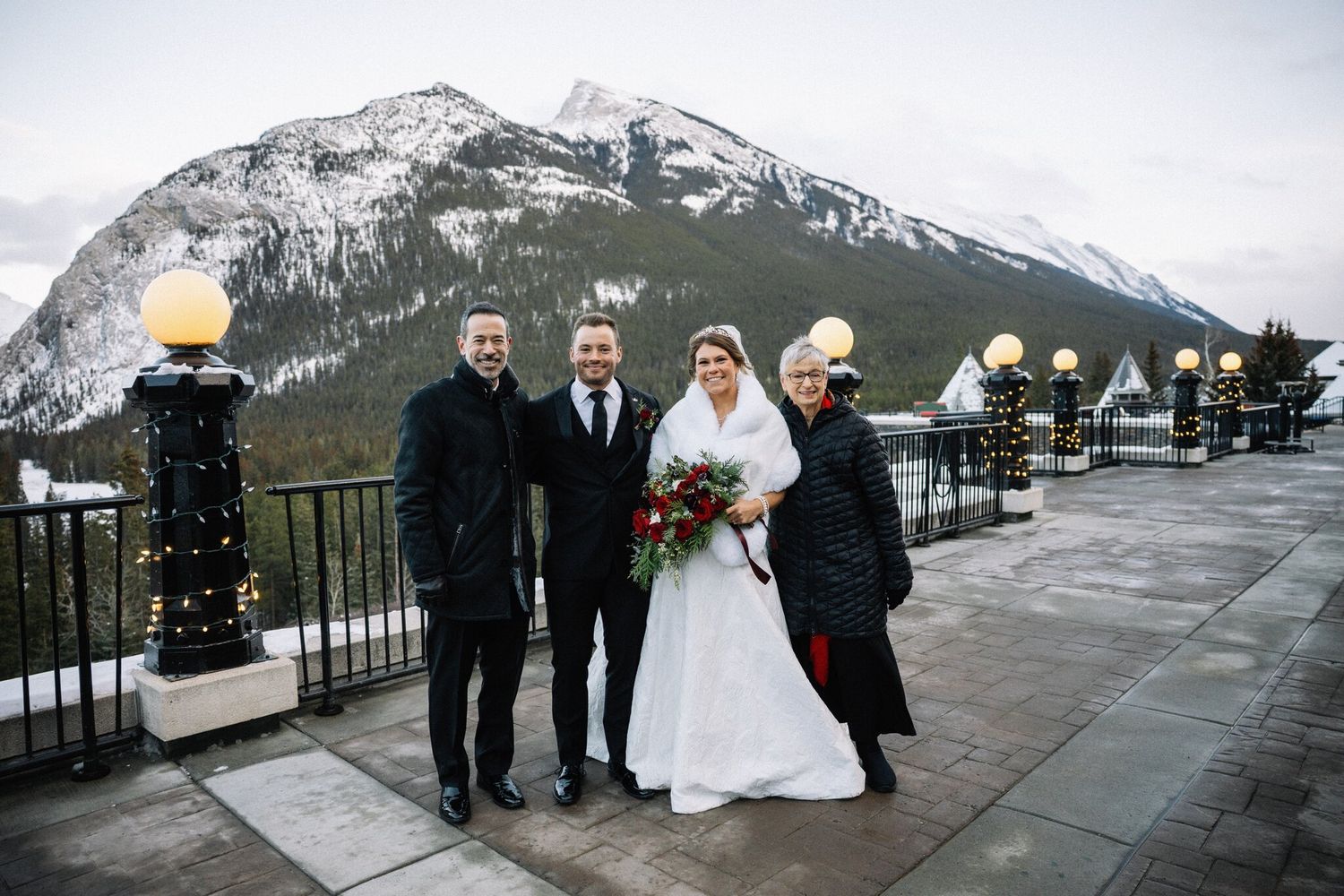 Bride and groom pose with family on a terrace lined with glowing lamp posts at their Banff winter wedding