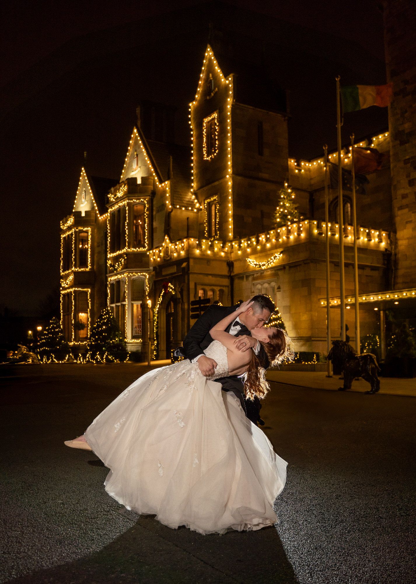 Bride and groom share a romantic dip kiss at night in front of a Clontarf Castle photography by Anthony Kane of AK Wedding photography