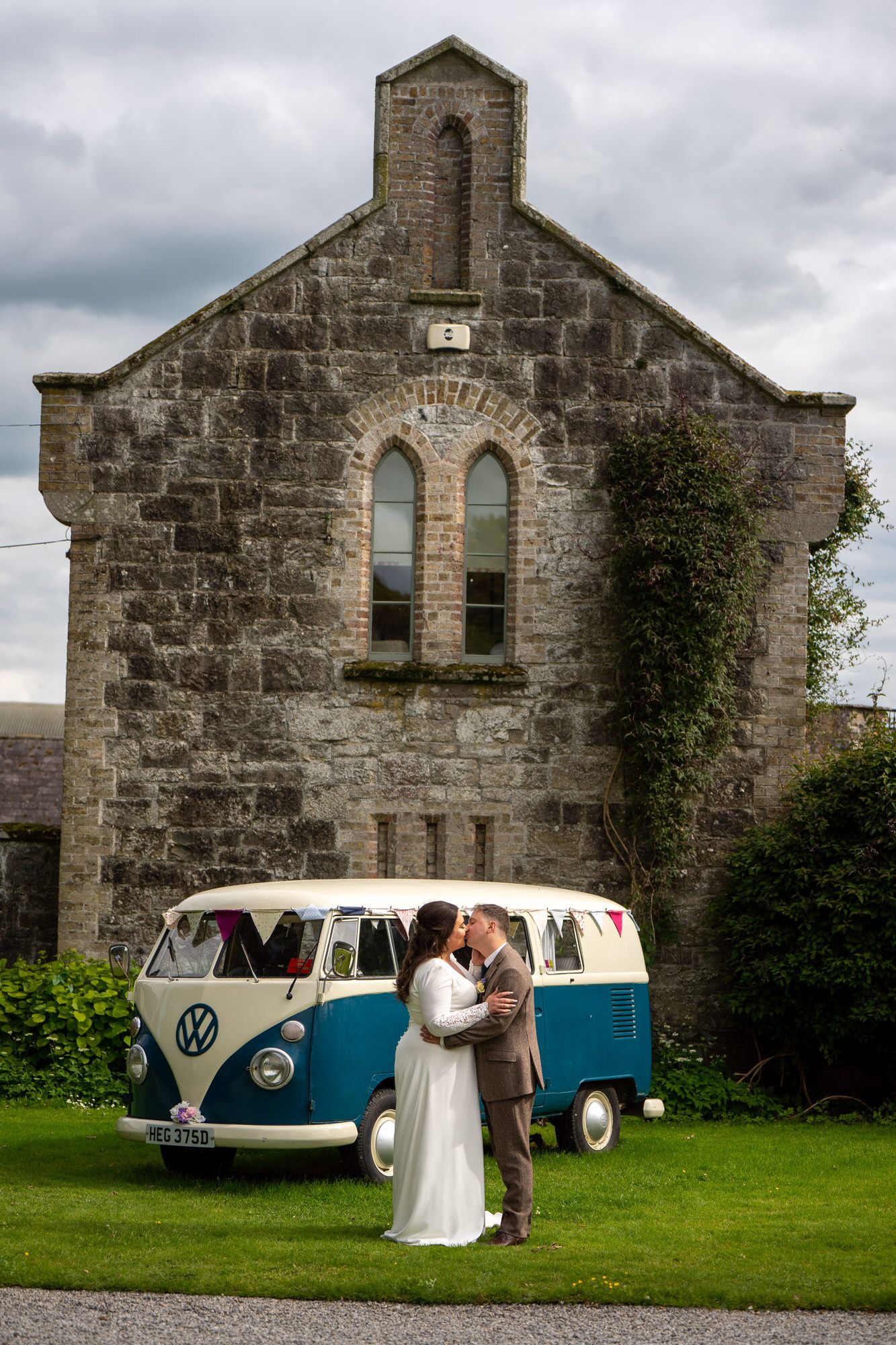 Bride and groom kissing in front of a vintage VW camper van on their wedding day at Martinstown house. Photo by AK wedding photography.