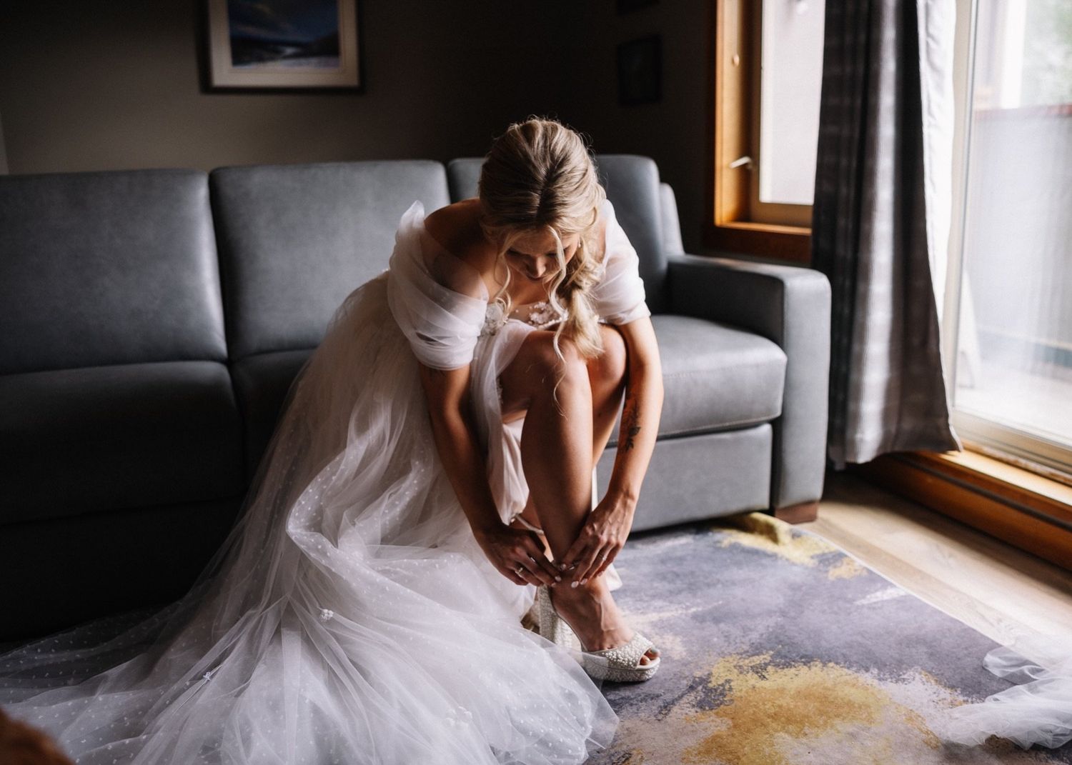Bride in an off-shoulder tulle gown putting on her shoes while getting ready for her Canmore wedding