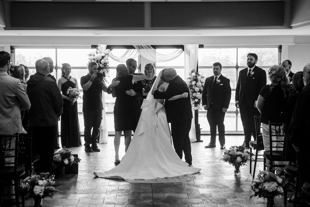 Black and white wedding ceremony photo showing bride and groom embracing at the altar with guests watching.