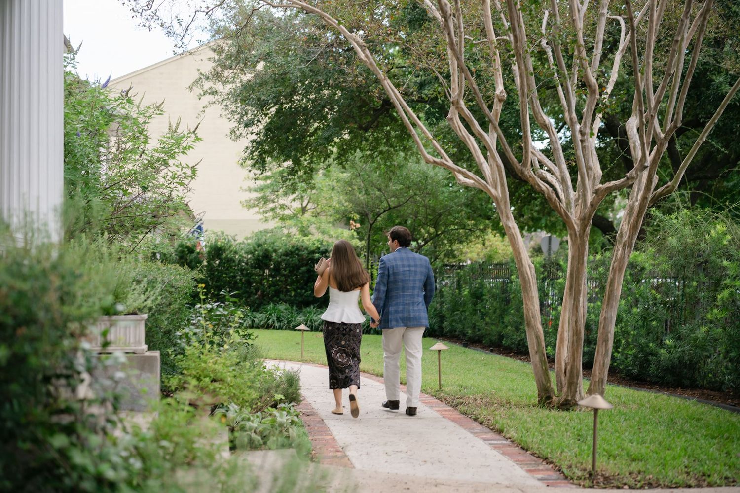 Man and woman holding hands walking down sidewalk.