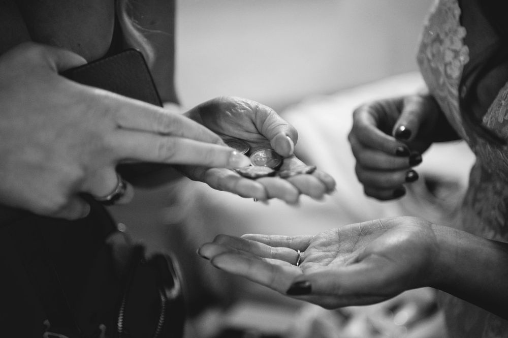 Black and white close-up of hands exchanging coins, with one open palm receiving money from another person's fingers.