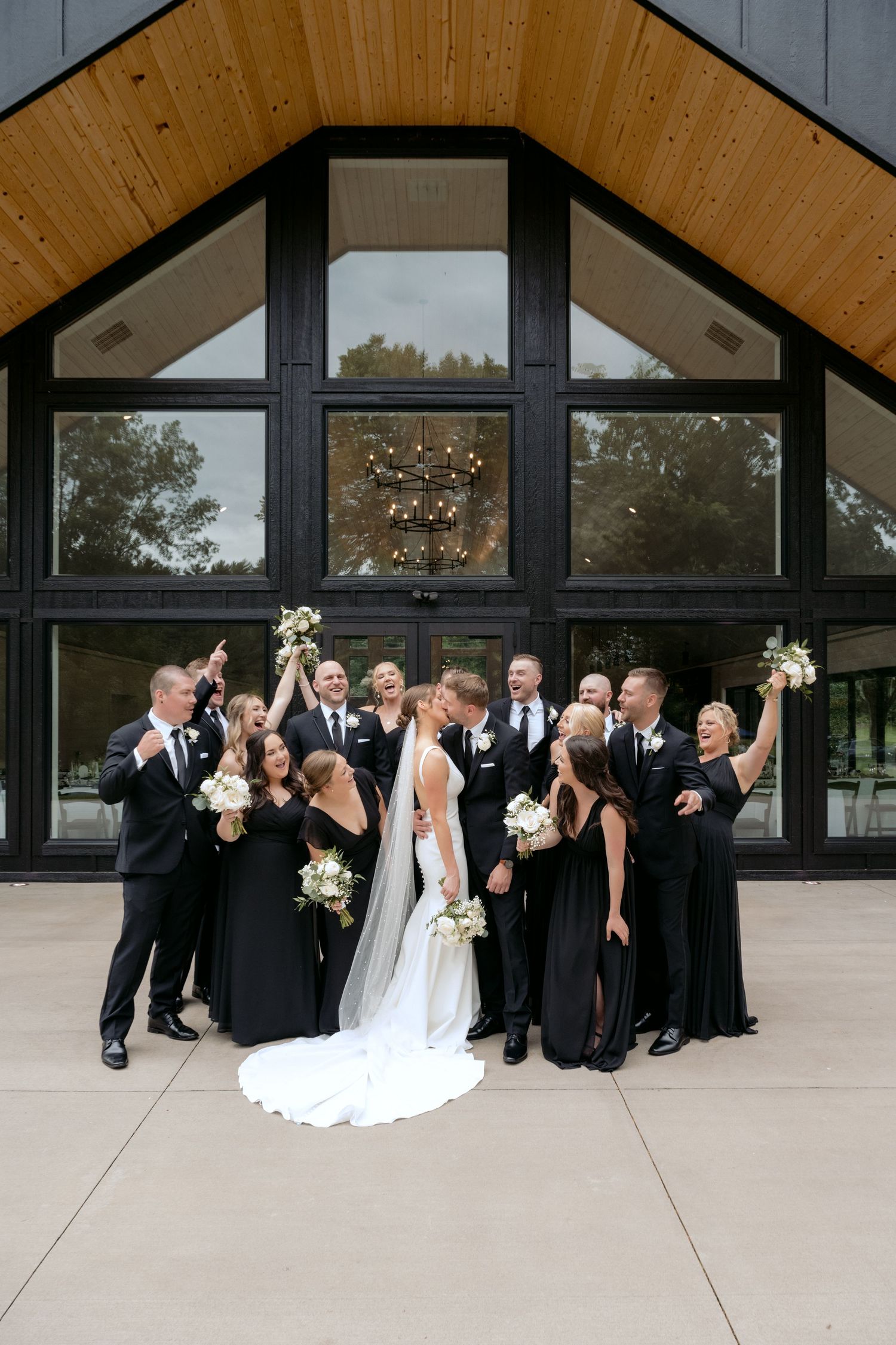 Full bridal party cheers as bride and groom kiss during bridal party portraits at La Pointe Events in Somerset, WI.